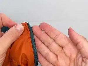 Place the top stop on the flat, tape side of the zipper, aligning the double-prong side of the stop to face the jacket and the single-prong side to face the zipper teeth.