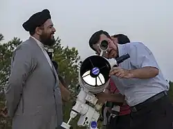 One man watches another, who looks through a modern telescope