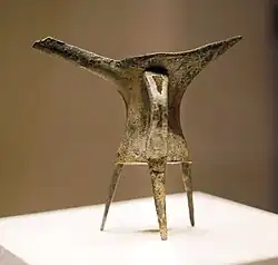 A thin bronze drinking vessel standing on a museum display stand