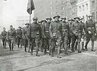 Black and white photo of soldiers lined up and marching in a street
