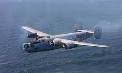 A four-engine military aircraft flying over a large body of water