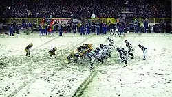 A snowy football field with Packers and Seahawks players lined up in formation.