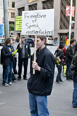 A man is holding a sign that reads "Freedom of speech, motherfuckers!"