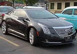 Front three-quarters view of a black 2-door coupe. Featuring a Cadillac badge, vertically-shaped headlights adorn its exterior. It has large wheels, and its license plate says Cadillac ELR, with the former word in an unusual font.