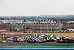 A plethora of cars turning left into a corner at the Circuit de la Sarthe