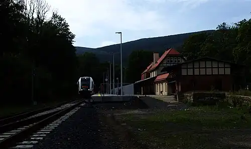 A train station with trees and a train coming.