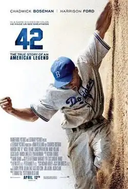 A man, wearing a baseball uniform, slides through the ground; The shot is tilted. Actors Chadwick Boseman and Harrison Ford are mentioned. Blue text says "Based on the True Story of an American Legend", as well as "In a game divided by color, he made us see greatness".