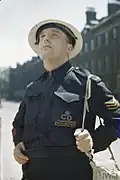 An ARP Warden for the London neighbourhood of Holborn surveys bomb damage in dark blue battledress.