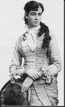 Black and white photo of a woman in 18th century dress holding a hat.