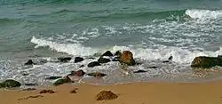 A beach with golden sand and large rocks along the shoreline