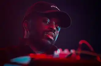 close-up of Alfa Mist wearing a ball cap, looking down at a DJ mixer