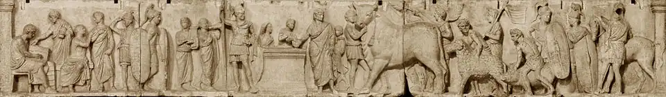 Relief depicts a long continuous scene that may be divided into three main groupings from left. The first is a group of four men wearing togas. Two are seated, and one is writing in a tablet. Two tall military guards divide this group from the central scene of sacrifice. Two musicians, markedly shorter than the soldiers, play a lyre and a horn. An unadorned altar, waist-high, stands in the center. To the viewer's left is the tallest figure in the composition, a military officer wearing a high plumed helmet and holding a long slender spear. standing by an altar. On the other side of the altar a priest, his head ritually covered, extends a libation bowl. A boy attendant pours from a pitcher into the bowl, and to that boy's right is a smaller boy looking on and lifting his right hand to the top of his head, a gesture that appears quizzical to modern viewers but may have some other significance in its Roman context. The priest is accompanied by a third boy close to his left side who stands ready with a towel. The right side of the relief is devoted to the procession of the three animal victims for the suovetaurilia, each led by a young male attendant, barechested but wearing a short kilt-like garment, with a wreath on his head. The first leads an enormous bull with a tasseled rope dangling from below its left horn. A fourth male attendant in the same attire follows closely on the bull's hindquarter, waving a palm branch in each hand. The attendant bringing the ram is followed by another veiled figure carrying a pole from which a banner unfurls. The attendant herding the pig is followed by another soldier bearing a long shield and looking back at another whose shield rests on the ground, covering most of his body. The last figure is a cavalryman, back turned to the viewer, next to his horse.