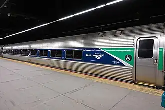 A silver railroad car with a blue stripe over the windows. At one end, an angular green shape covers the stripe.