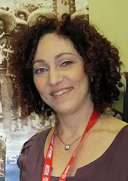 A woman with curly red hair standing behind a desk greetin people