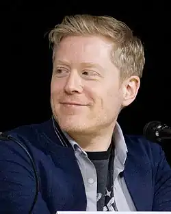 An informal bust photograph of a blond white man smiling and looking to his right