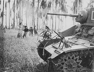 7 January 1943. Australian forces attack Japanese positions near Buna. Members of the 2/12th Infantry Battalion advance as Stuart tanks from the 2/6th Armoured Regiment attack Japanese pillboxes. An upward-firing machine gun on the tank sprays treetops to clear them of snipers. (Photographer: George Silk).