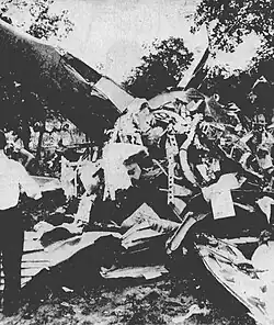 A man stands next to a pile of aircraft wreckage
