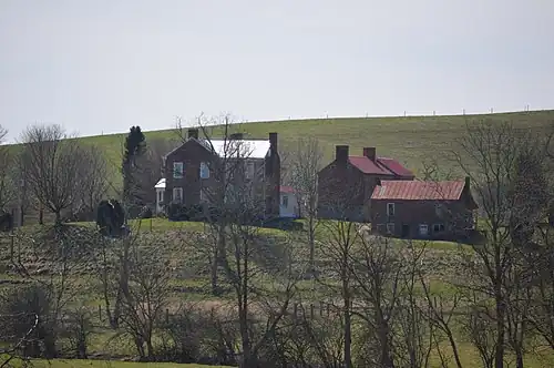 A color photograph of three buildings behind some trees and in front of a green mound