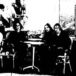 A very grainy black and white photo of the band seated at a table
