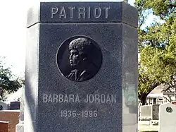 Barbara Jordan's gravestone at the Texas State Cemetery in Austin, Texas. Picture is of Jordan's gravestone which includes the word "patriot" carved at the top followed by an engraving of Jordan's profile.