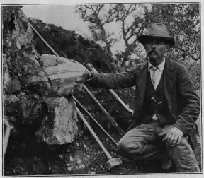 William E. Hidden next to a 73 lb (33 kg) mass of gadolinite in place at Barringer Hill, 1903.