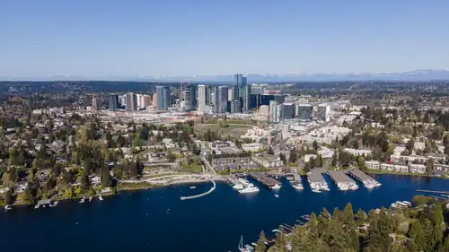 Aerial view of a lakefront park and covered boat docks with high-rise buildings in the background