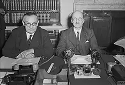 Two men sit side by side at a desk.