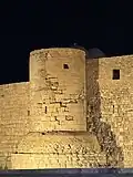 A close-up of one of the fortress towers illuminated at night, highlighting its architectural details