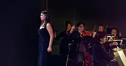 Soprano Megan Marie Hart is standing in front of the Bourbon Baroque period instrument orchestra. Violinist Nicolas Fortin has raised his bow, harpsichordist John Austin Clark's hands are hovering above the keys.