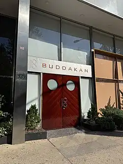 Dark reddish double doors with a handle in the shape of a capital letter B. A silver awning with "Buddakan" in spaced out capital letters.