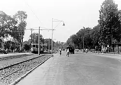 A photograph with a streetcar on the left and a city street with pedestrians crossing on the right