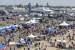 An aerial view of the 2023 California Capital Airshow, with a large crowd and static displays of military aircraft and exhibitors.