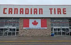 The facade of a Canadian Tire with a banner reading "Canadian owned and operated" on a Canadian flag