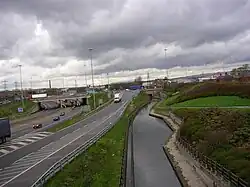 View from a bridge over a canal, with a motorway running to the left. The sky is dark and overcast.