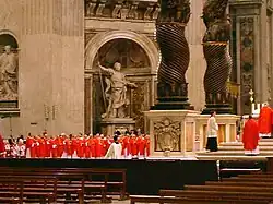 The cardinals, all in bright red robes, are grouped near the baldachin.