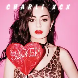 Charli XCX holds a red heart-shaped lollipop with the album's name written on it. She stands in front of a pink background and wears a leopard print tank top.