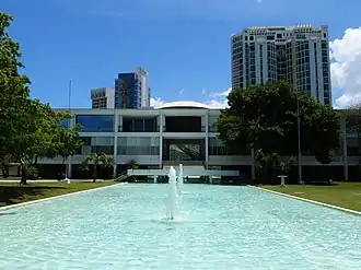 Photograph of the Supreme Court Building, a bright white building of three stories with an open space below, overtopped by a shallow dome