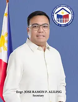 Aliling in 2025, wearing a Barong Tagalog with a pin on the collar, holding a maroon folder