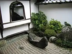 A wall with window and a raked stone garden.