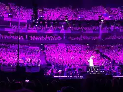 David Lawrence conducting the Young Voices children's choir, he is wearing a white suit and the choir is lit in purple.