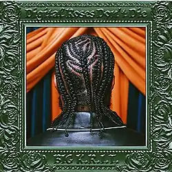 A photo of a Black man's head showing his braided hair. He's stood in front of blue and orange curtains, and the photo is surrounded by an ornate green photo frame.