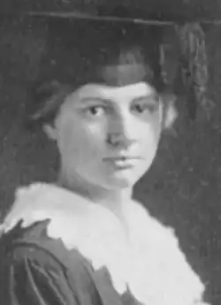 A young white woman wearing an academic mortar-board cap and a white lace-trimmed collar over an academic gown