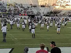 UCF football players, wearing black jerseys, going though warmups