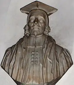 A stone bust of a man (head and shoulders), with beard, cap and robes