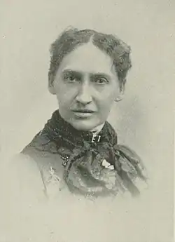 B&W portrait photo of a middle-aged woman with her hair in an up-do, wearing a dark, high-collared blouse.