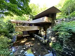 The house as seen from the access bridge across Bear Run stream. The main portion of the house is to the right of the stream, and the living room juts out over the stream at the center.