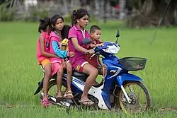 Young girl riding a motorcycle in the rice fields of Don Det, Laos, with four other children passengers.