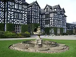 a stone fountain in front of a house painted black and white to resemble a half-timbered appearance