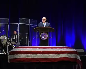 Larry Hogan speaking at a podium behind Holley's coffin, which is draped with a U.S. flag.