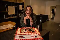 Kearney smiling while standing over a cake. The cake is decorated in Labor party colours, and features a picture of Kearney.